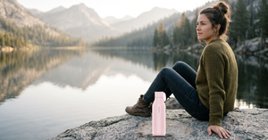 Woman by a mountain lake with a light pink water bottle on the rock